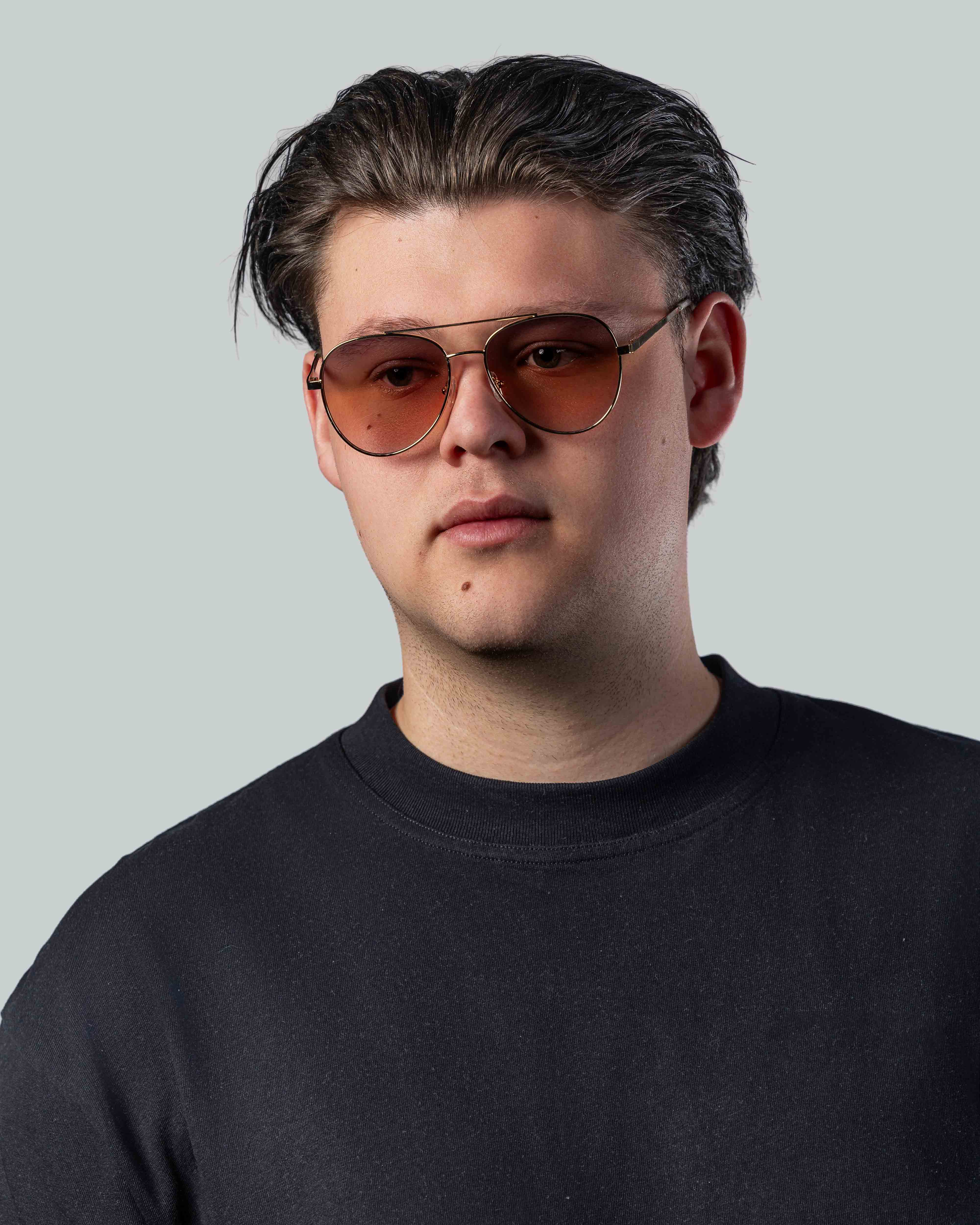 Man met stijlvolle zonnebril met gouden montuur en oranje glazen, perfect voor een trendy look.