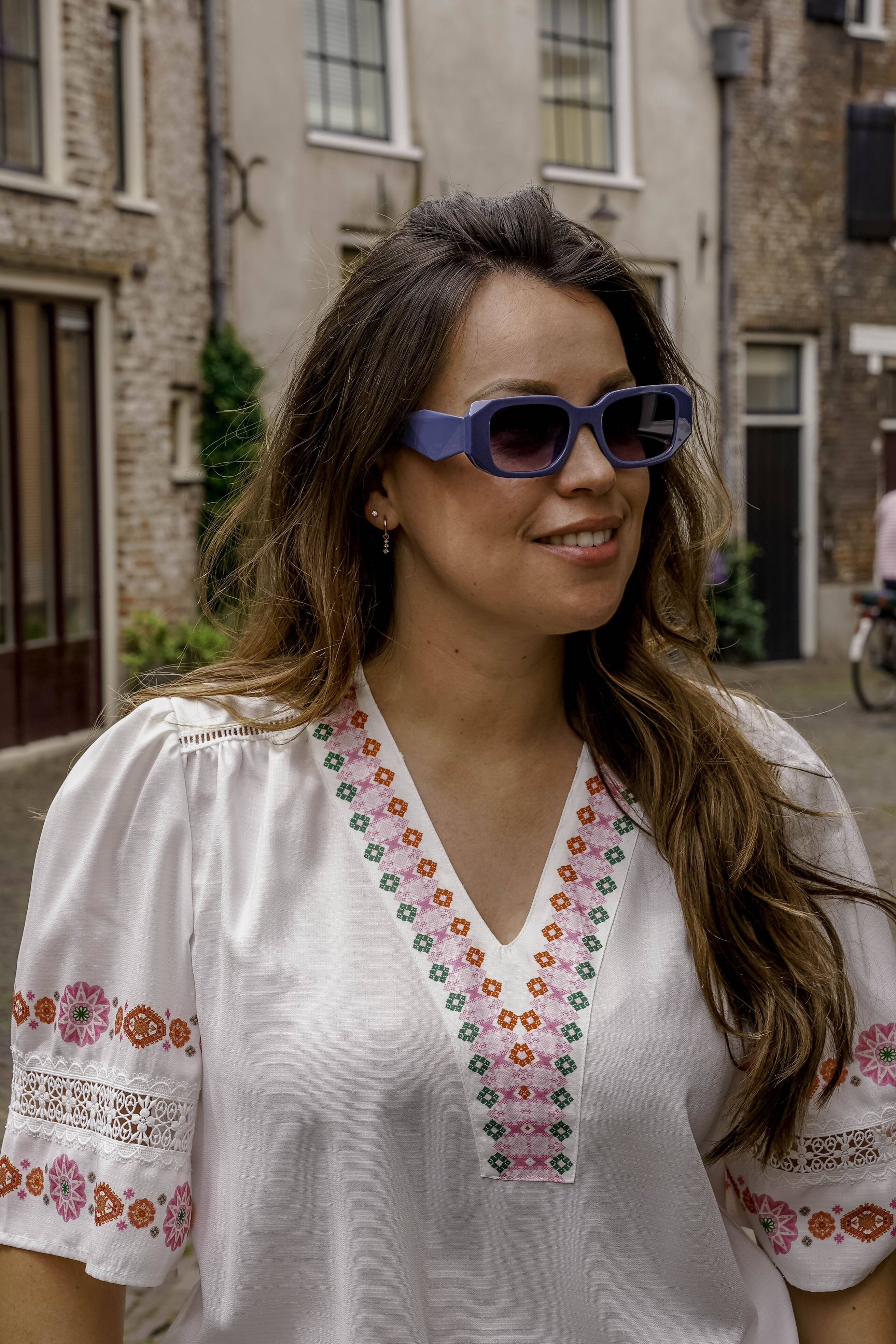 Vrouw met stijlvolle paarse zonnebril en geborduurde witte blouse op straat