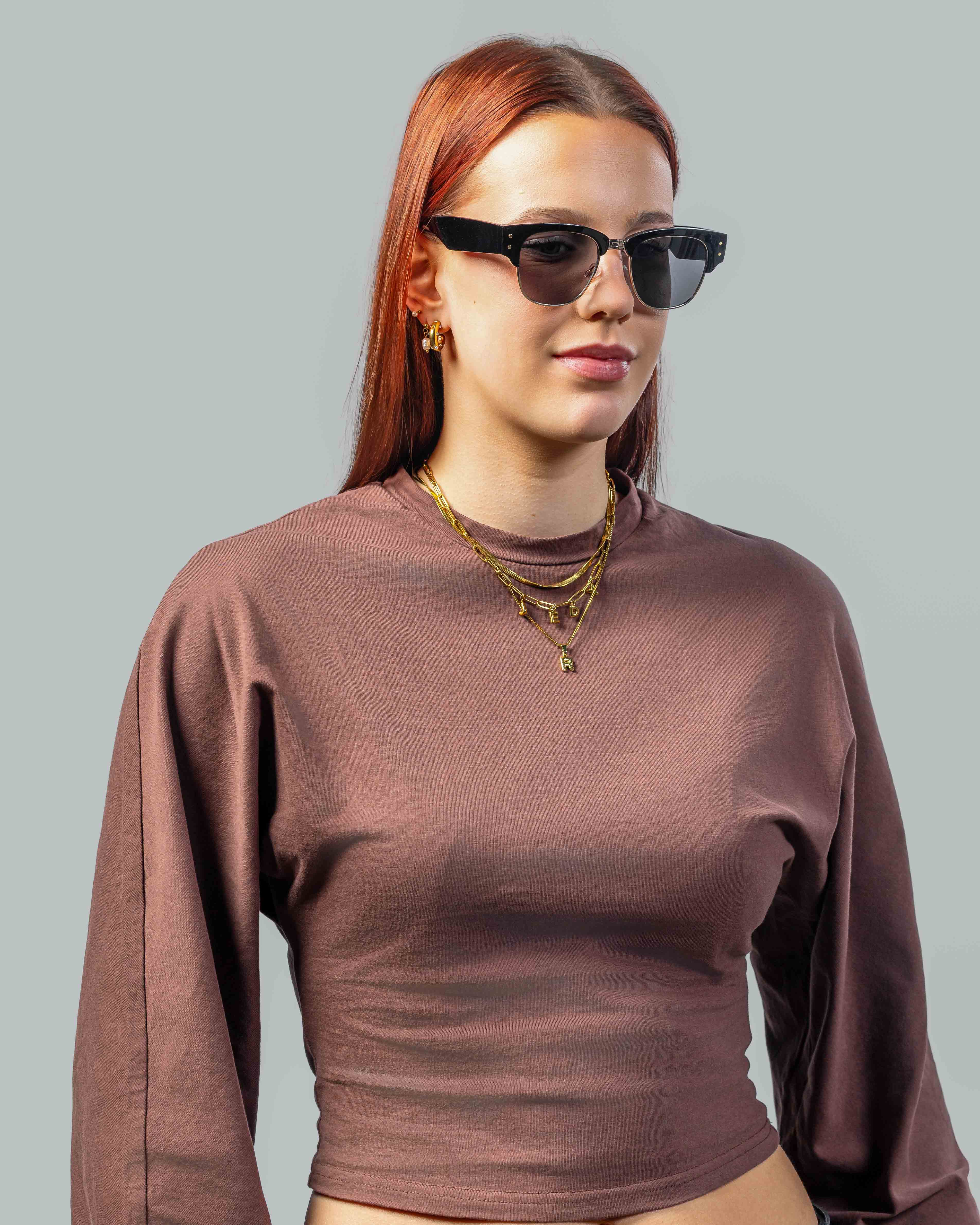 Stijlvolle zonnebril met zwarte montuur en donkere glazen, gedragen door vrouw met rood haar en gouden sieraden.