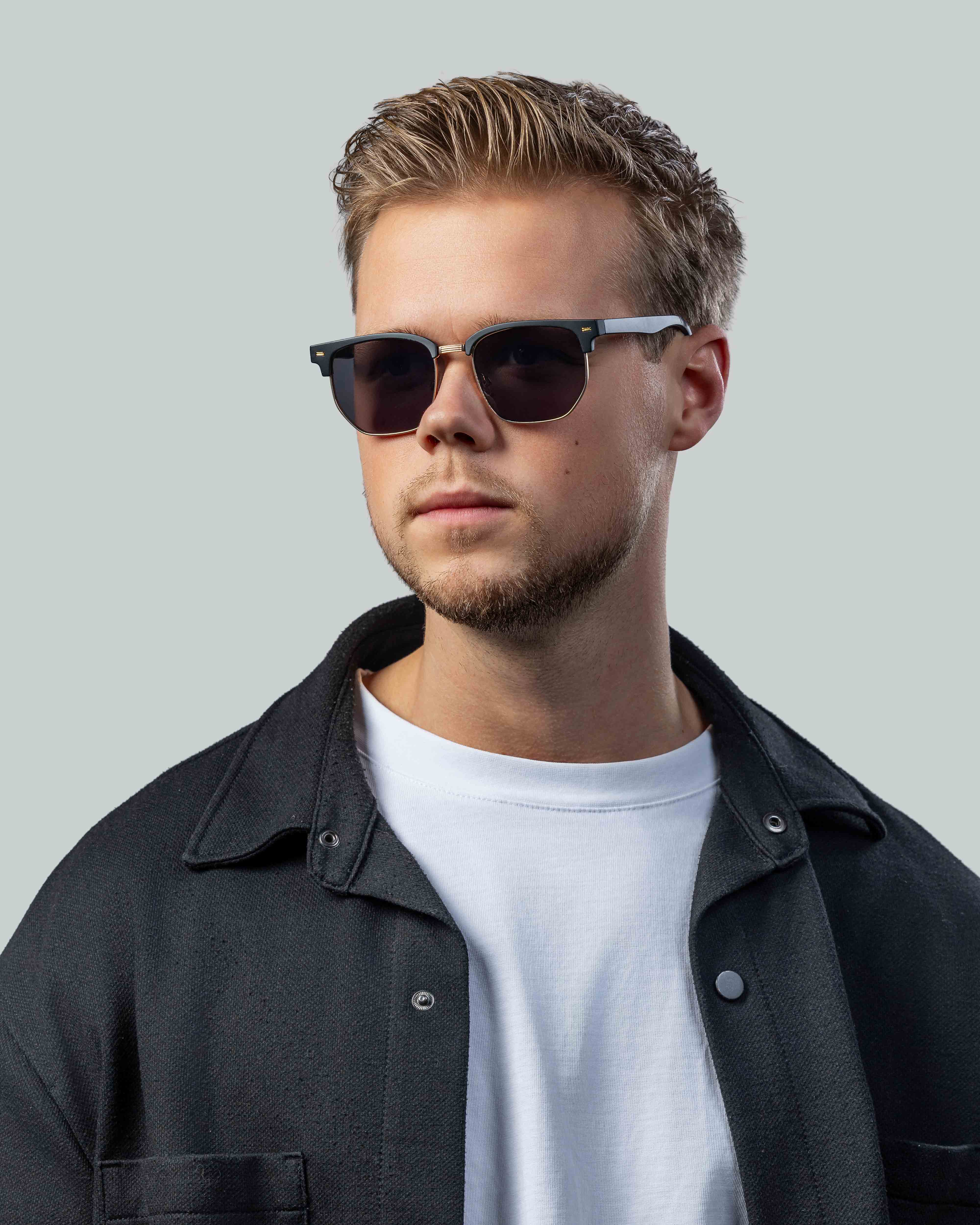 Stijlvolle zonnebril met donkere glazen en gouden accenten, gedragen door man in casual outfit