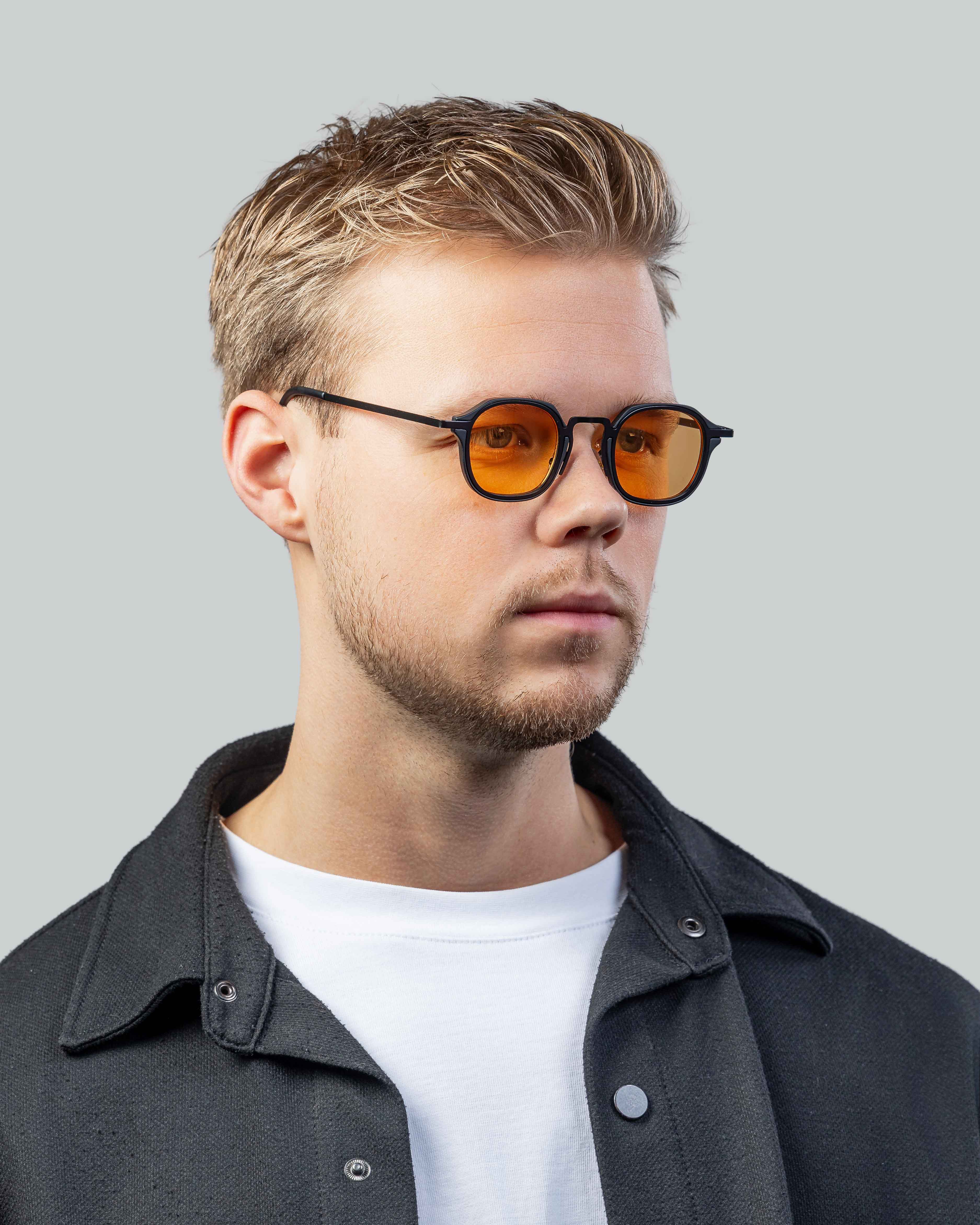 Stijlvolle zonnebril met oranje glazen en zwarte montuur, gedragen door man in casual outfit