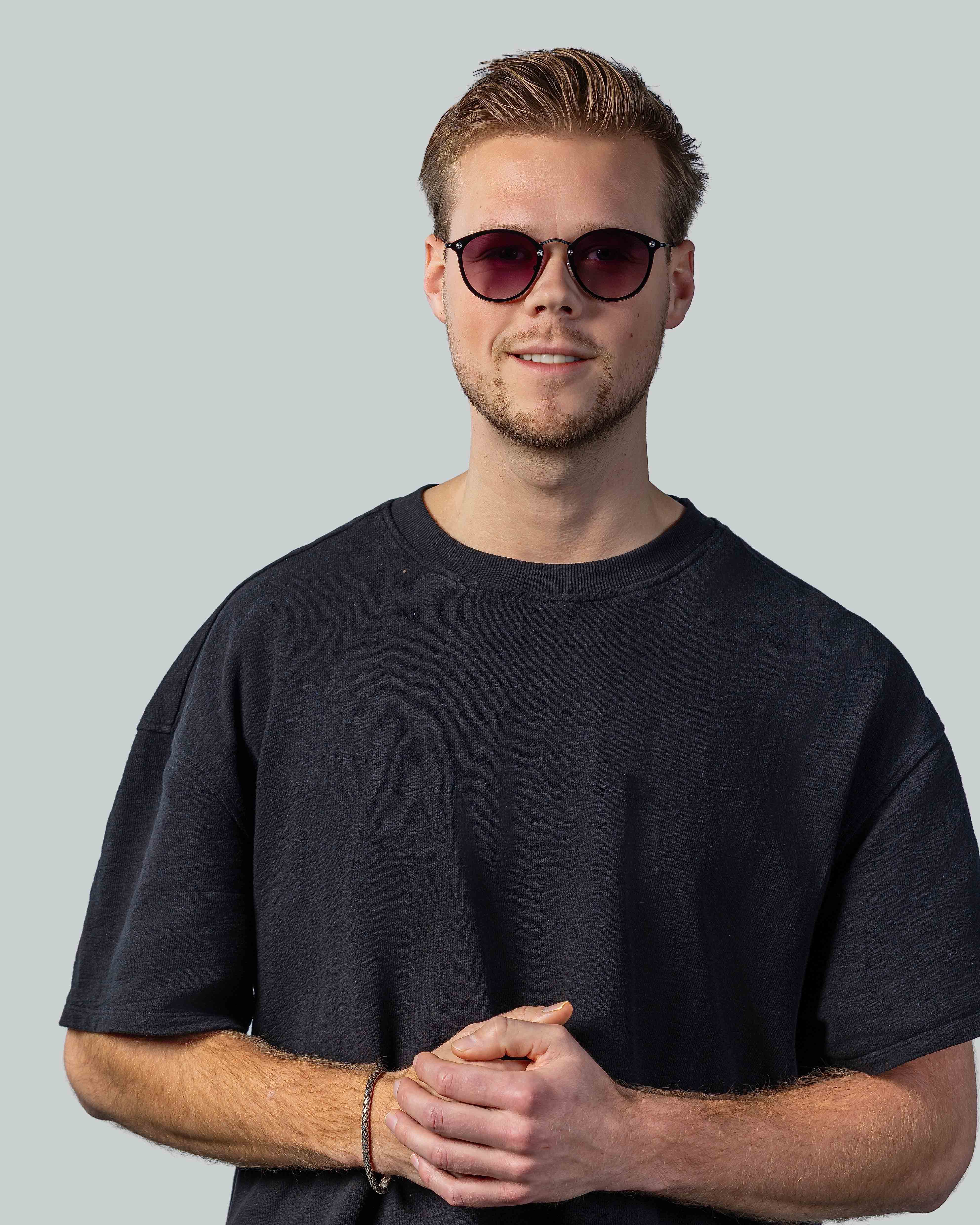 Stijlvolle zonnebril met roze glazen en zwarte montuur, gedragen door man in donkere t-shirt