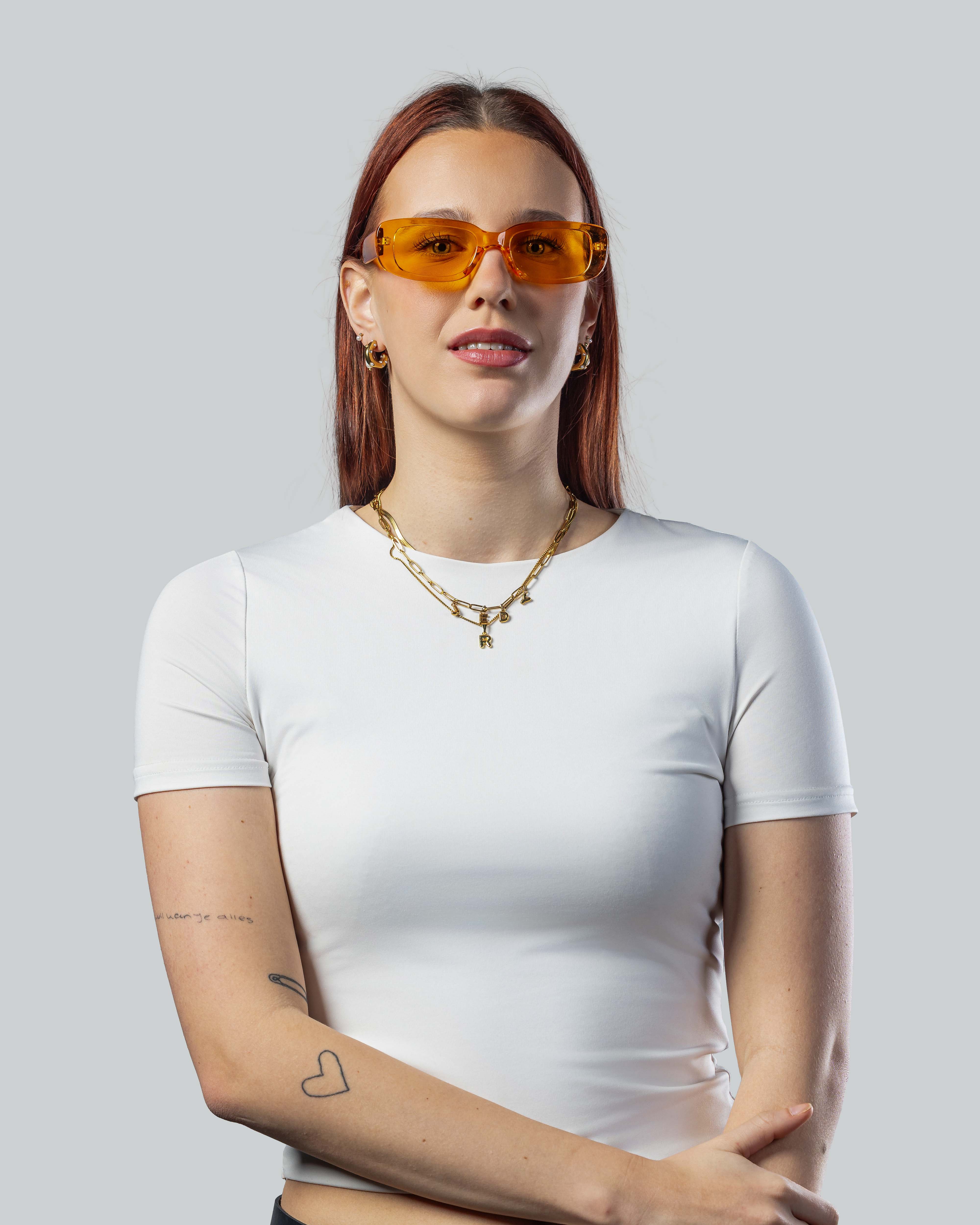 Vrouw met stijlvolle oranje zonnebril en witte top, perfect voor een trendy look.