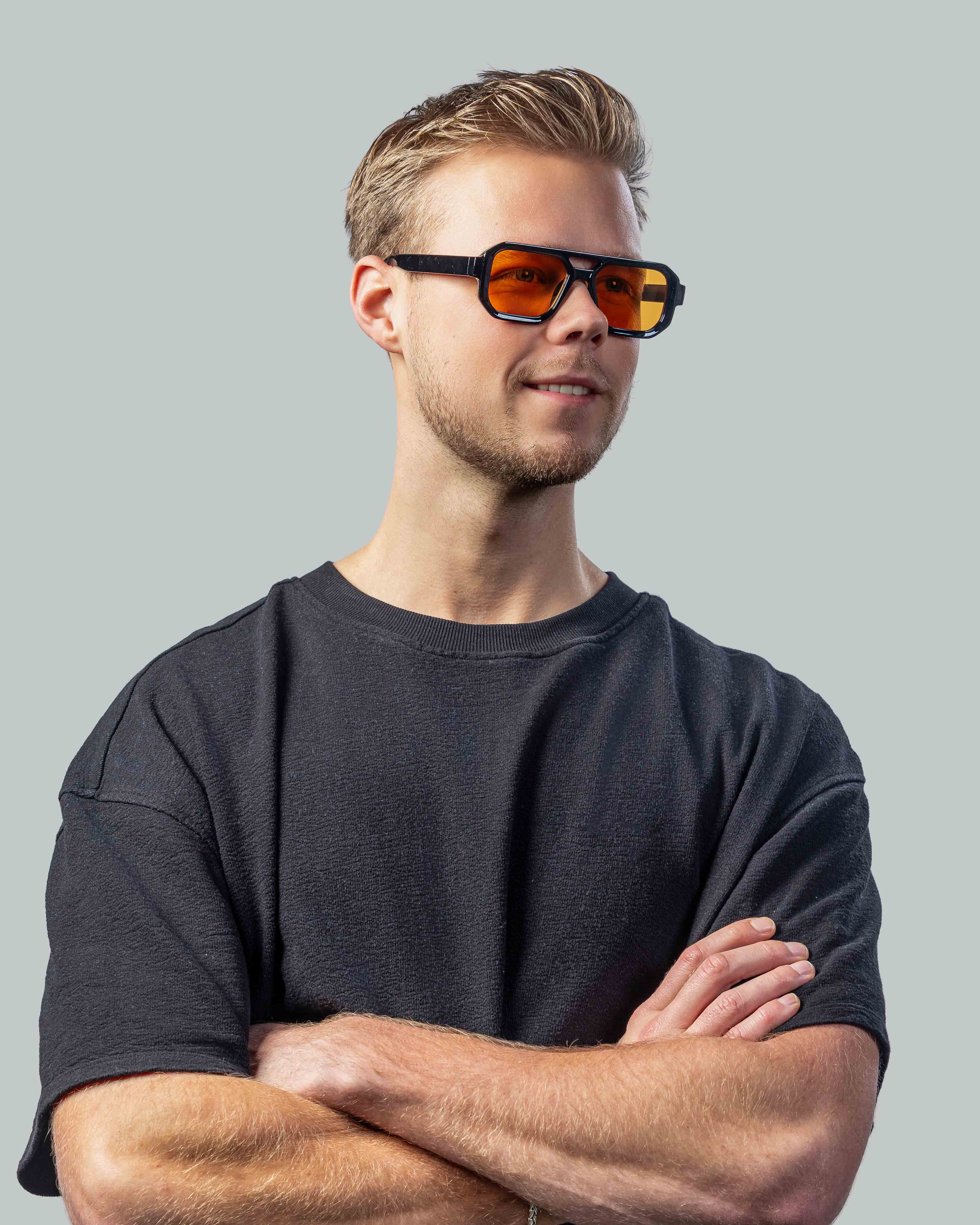 Stijlvolle zonnebril met oranje glazen en zwarte montuur, gedragen door man in donkergrijs shirt