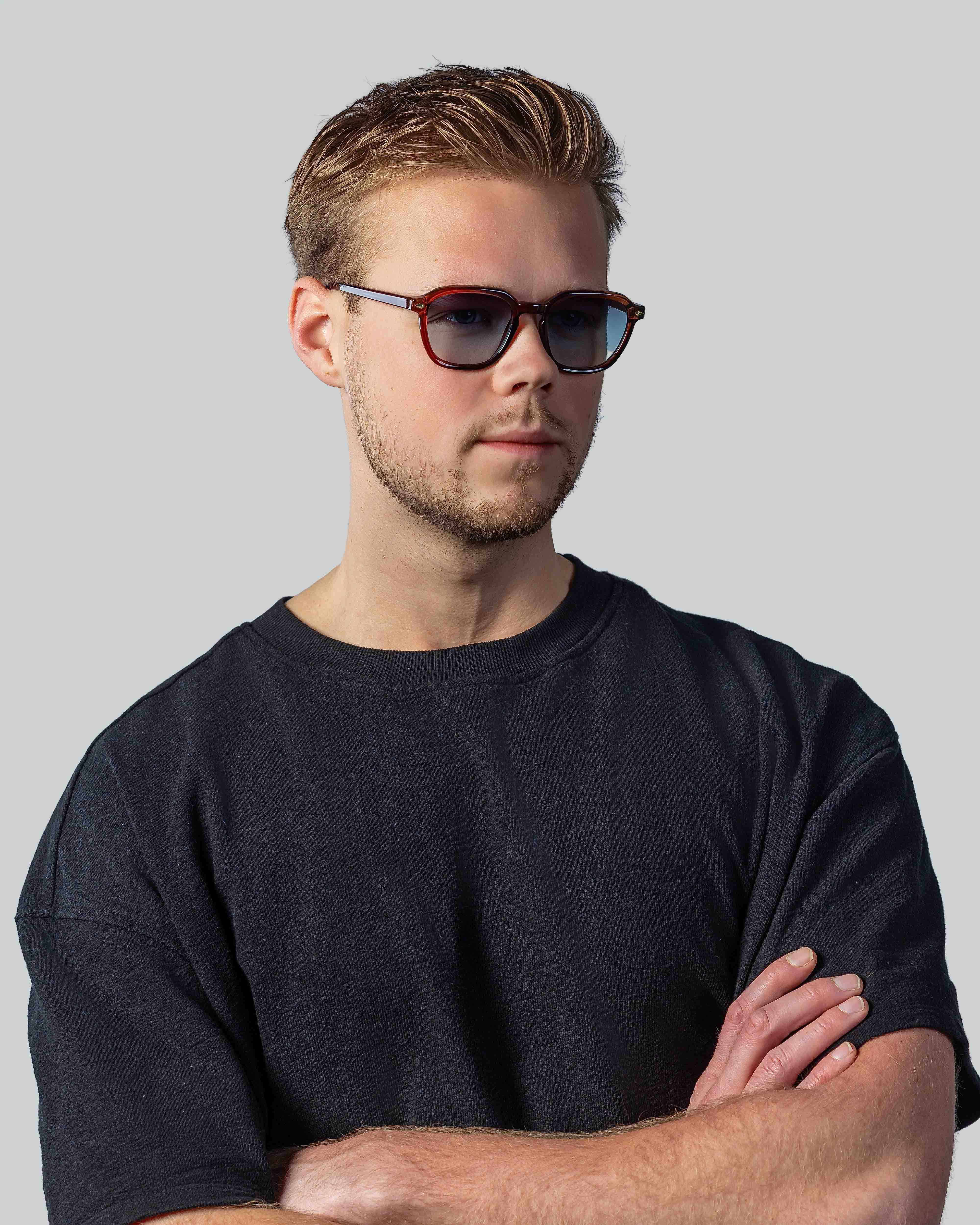 Stijlvolle zonnebril met bruine montuur en blauwe glazen, gedragen door man in zwart shirt