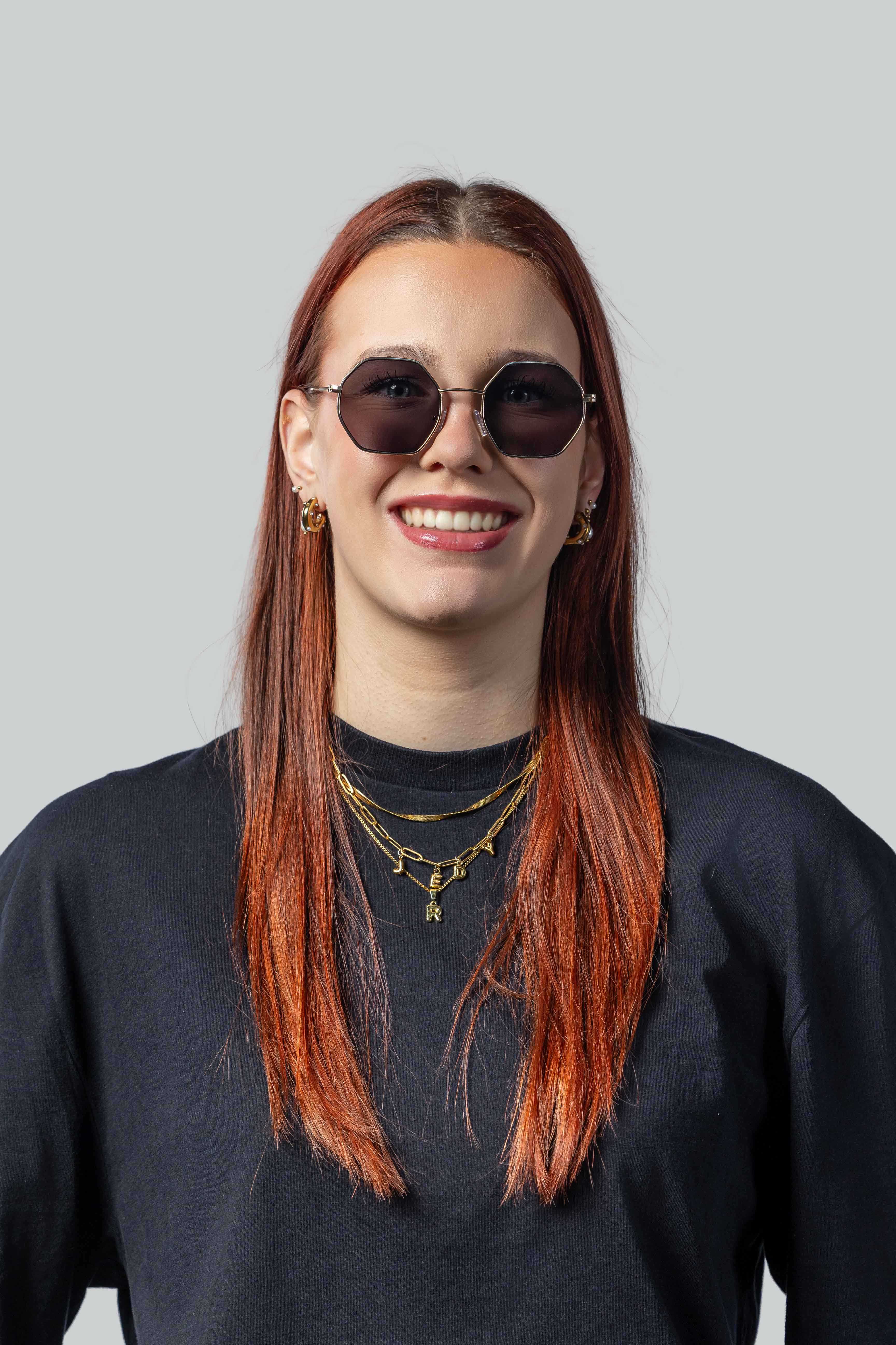 Vrouw met stijlvolle zonnebril, gouden sieraden en rood haar, perfect voor een modieuze look.