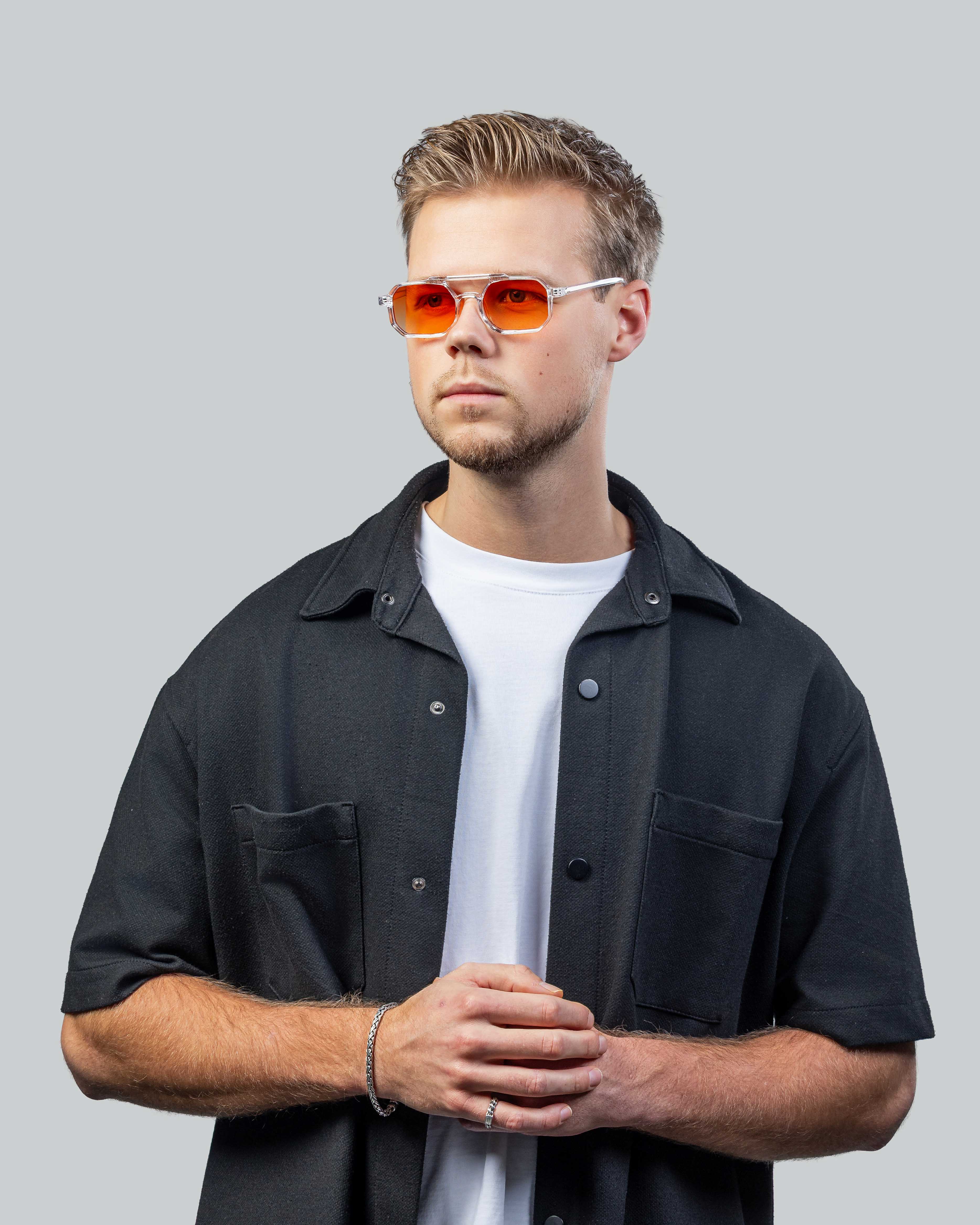Stijlvolle zonnebril met oranje glazen en transparant montuur, gedragen door man in casual outfit