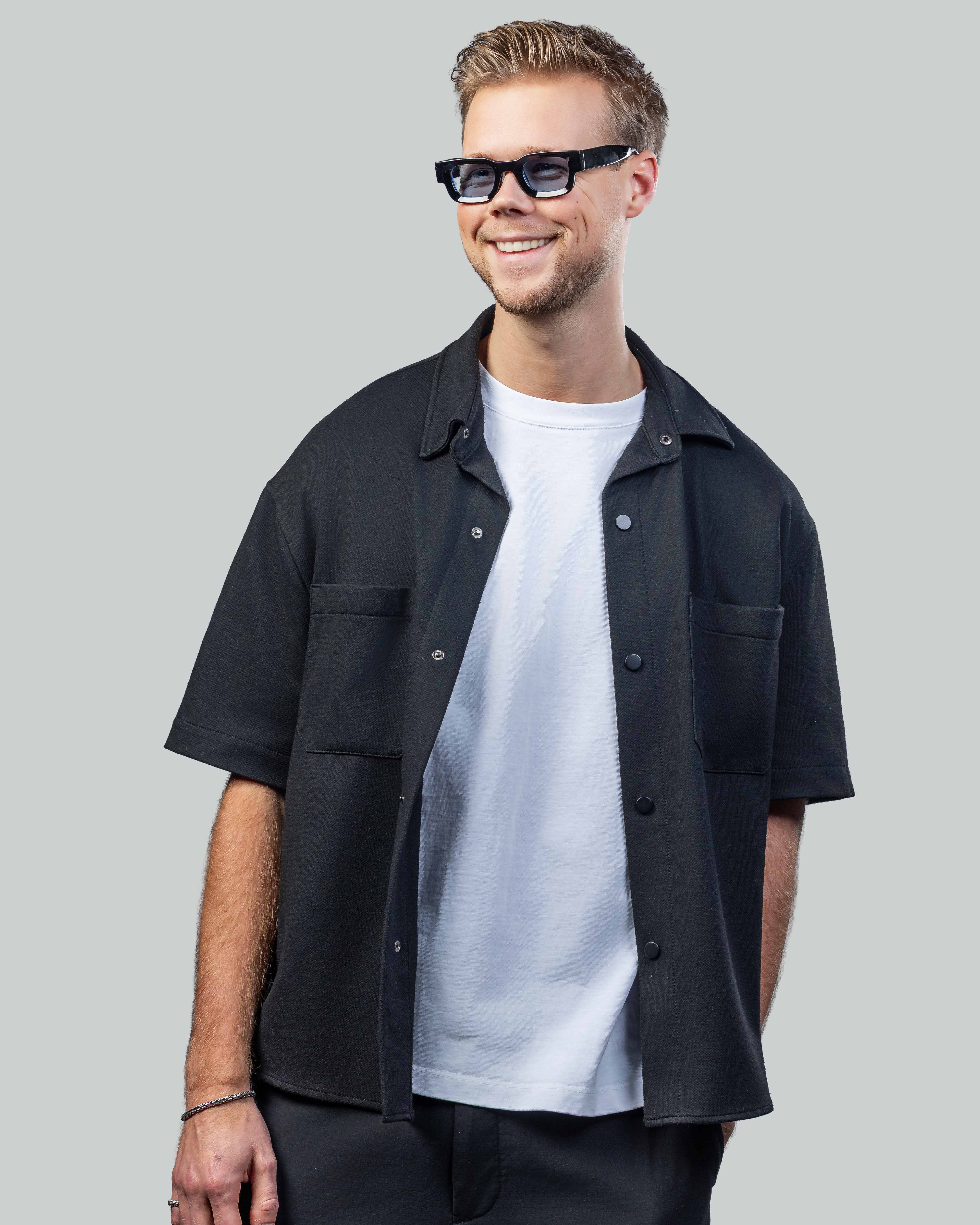 Man met stijlvolle zonnebril, zwarte shirt en witte t-shirt, perfect voor een moderne look.