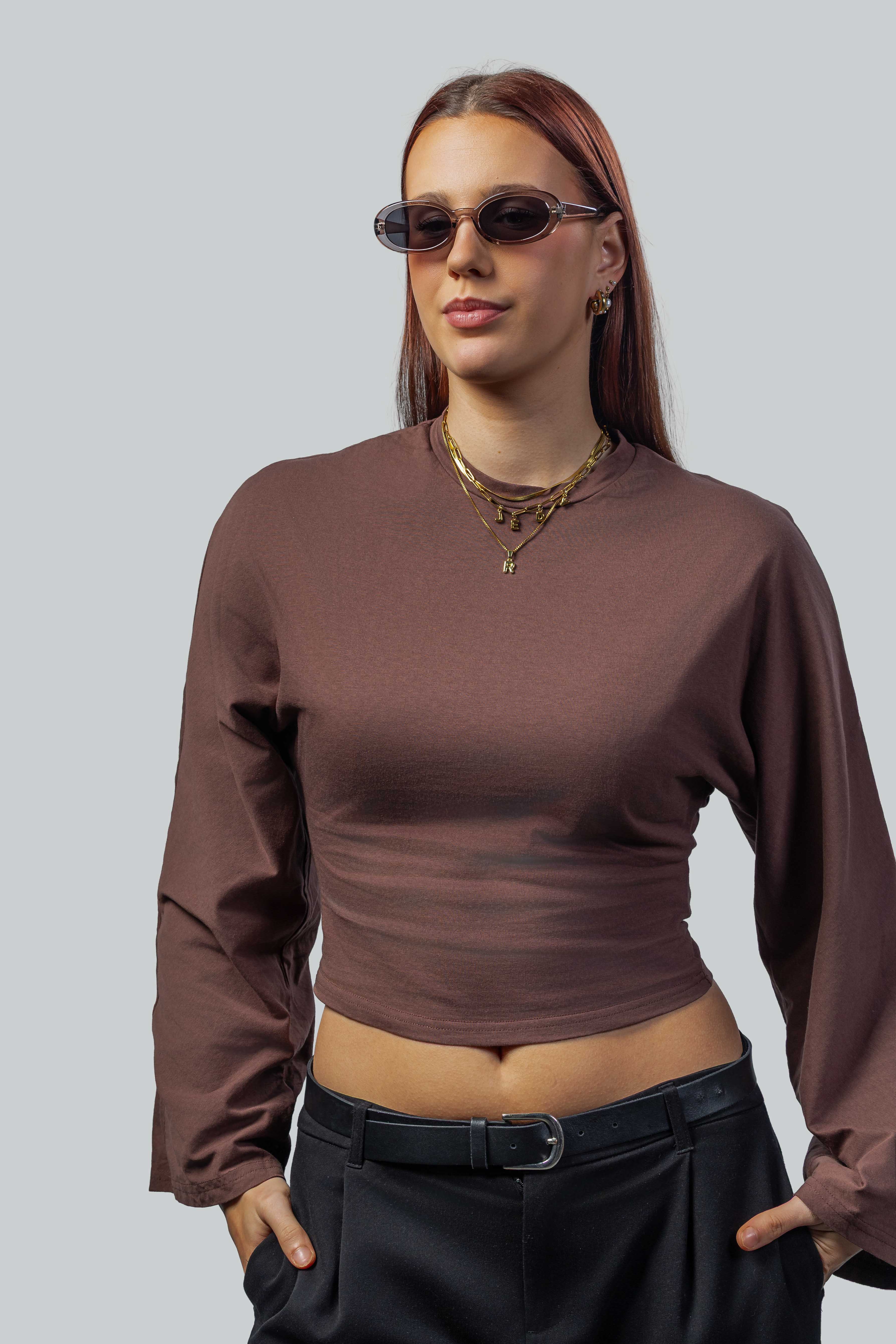 Stijlvolle ovale zonnebril met donkere glazen, gedragen door vrouw in bruine crop top en zwarte broek