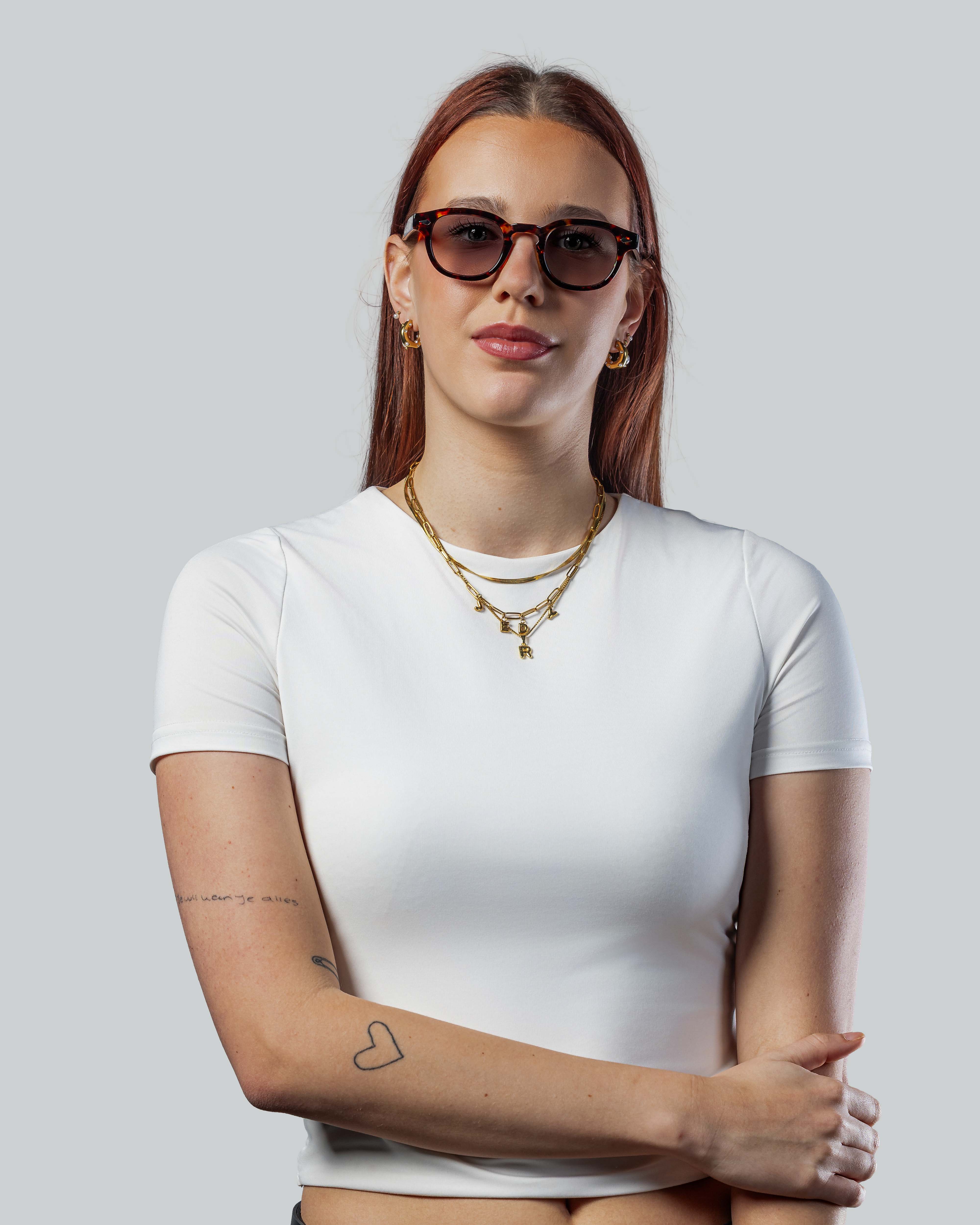 Vrouw met stijlvolle zonnebril, witte top en gouden sieraden, perfect voor een trendy look.