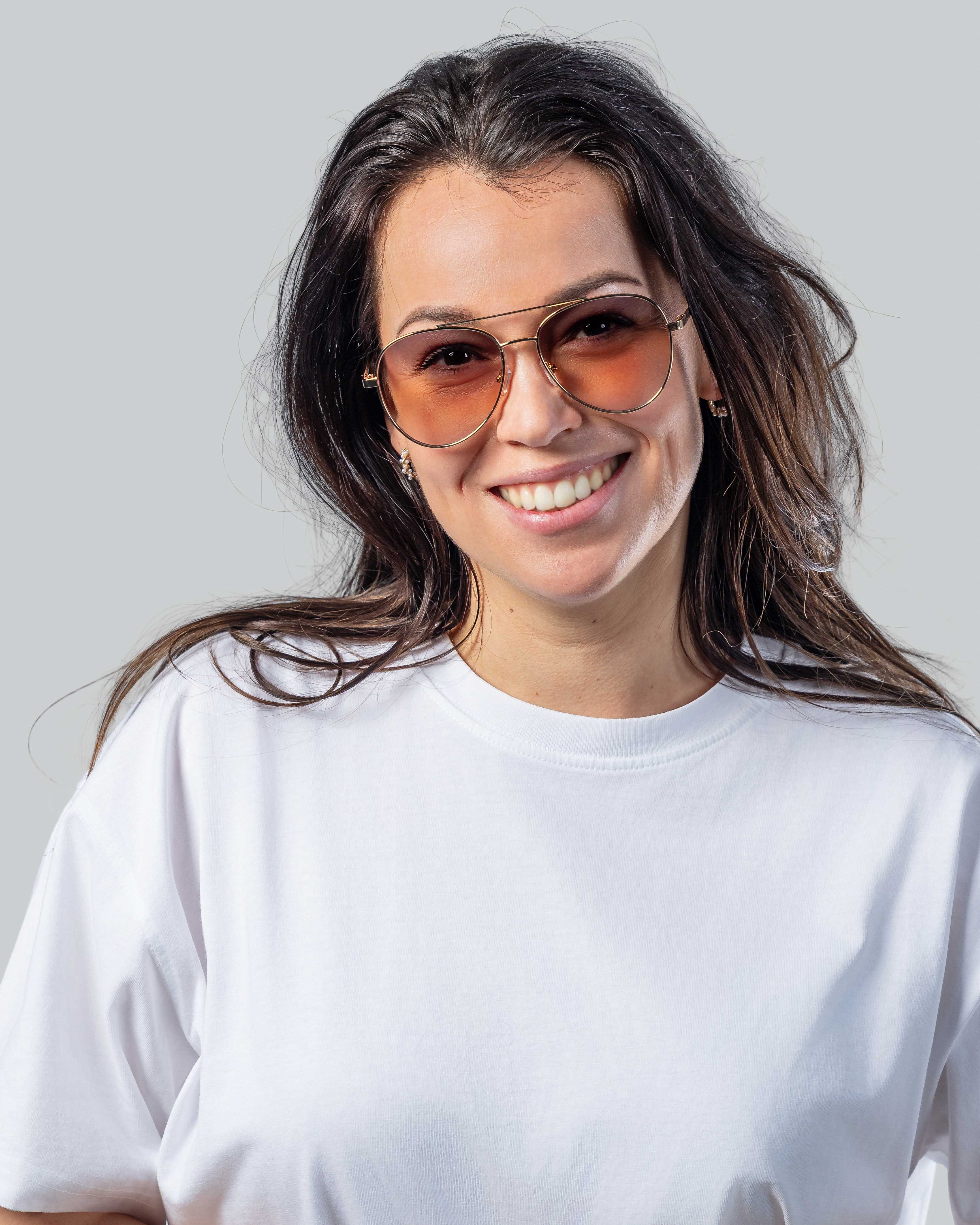 Vrouw met stijlvolle zonnebril met gouden montuur en roze glazen, perfect voor een zonnige dag