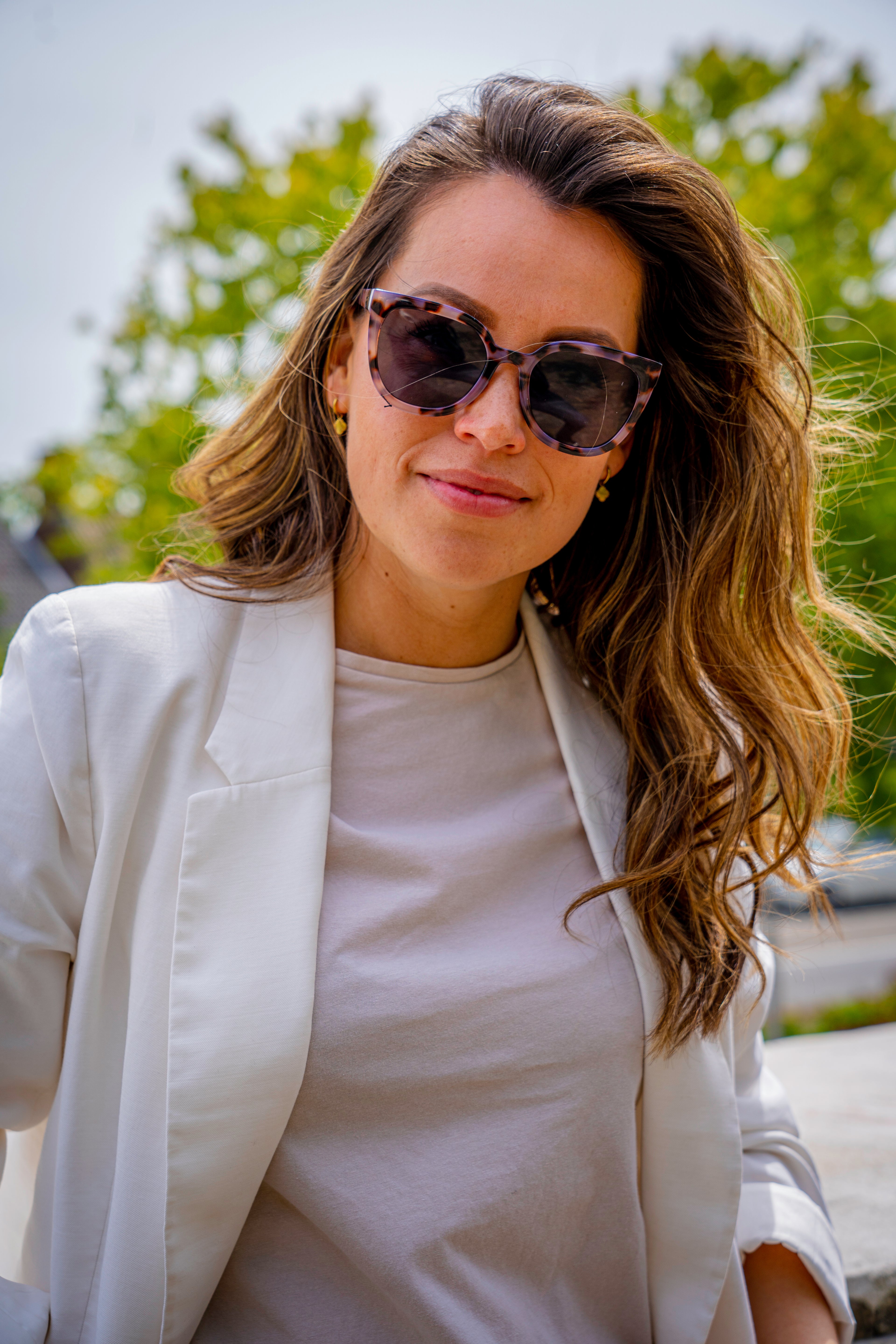 Vrouw met stijlvolle zonnebril, witte blazer en t-shirt, perfect voor zonnige dagen
