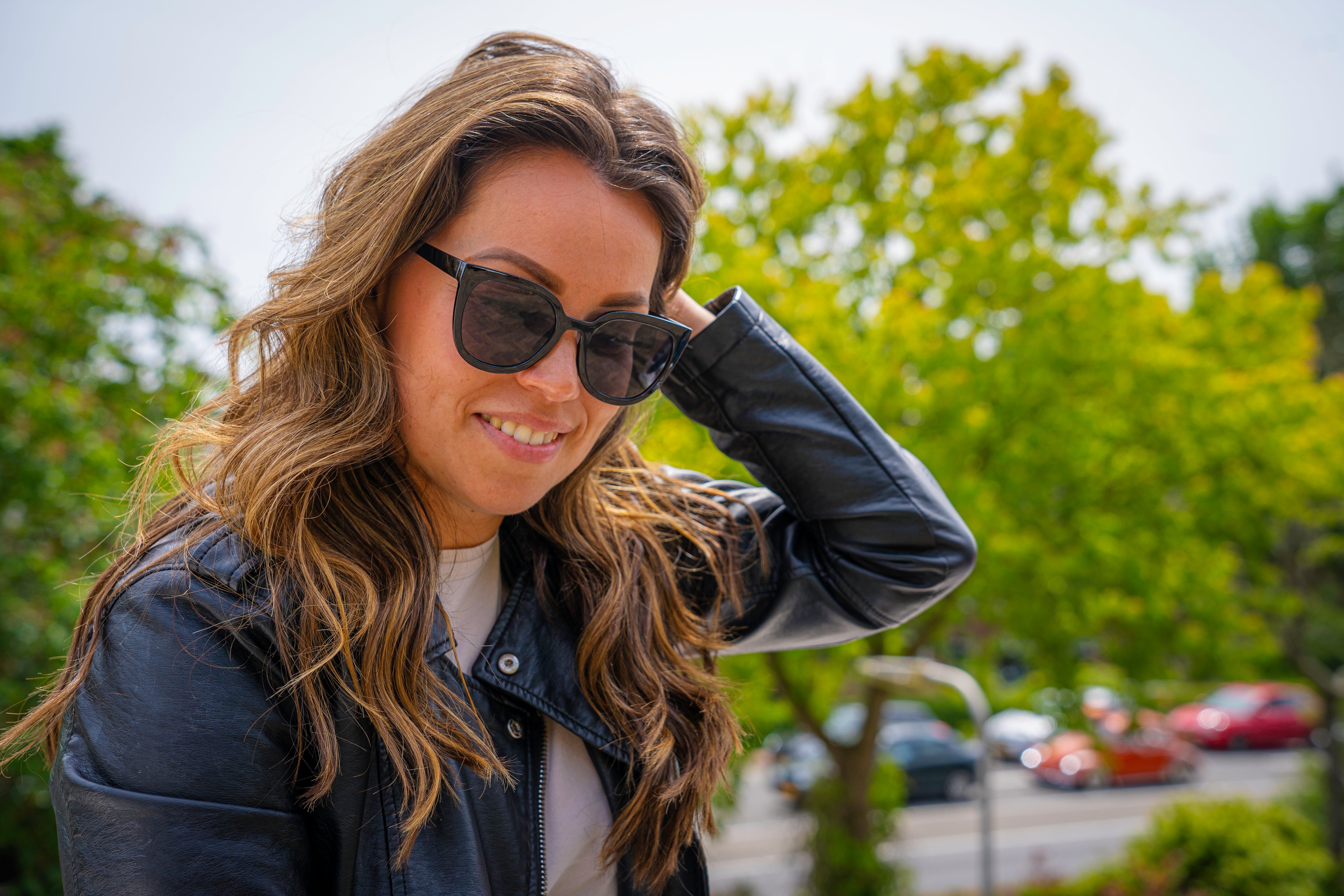 Vrouw met stijlvolle zonnebril en zwarte lederen jas in de natuur