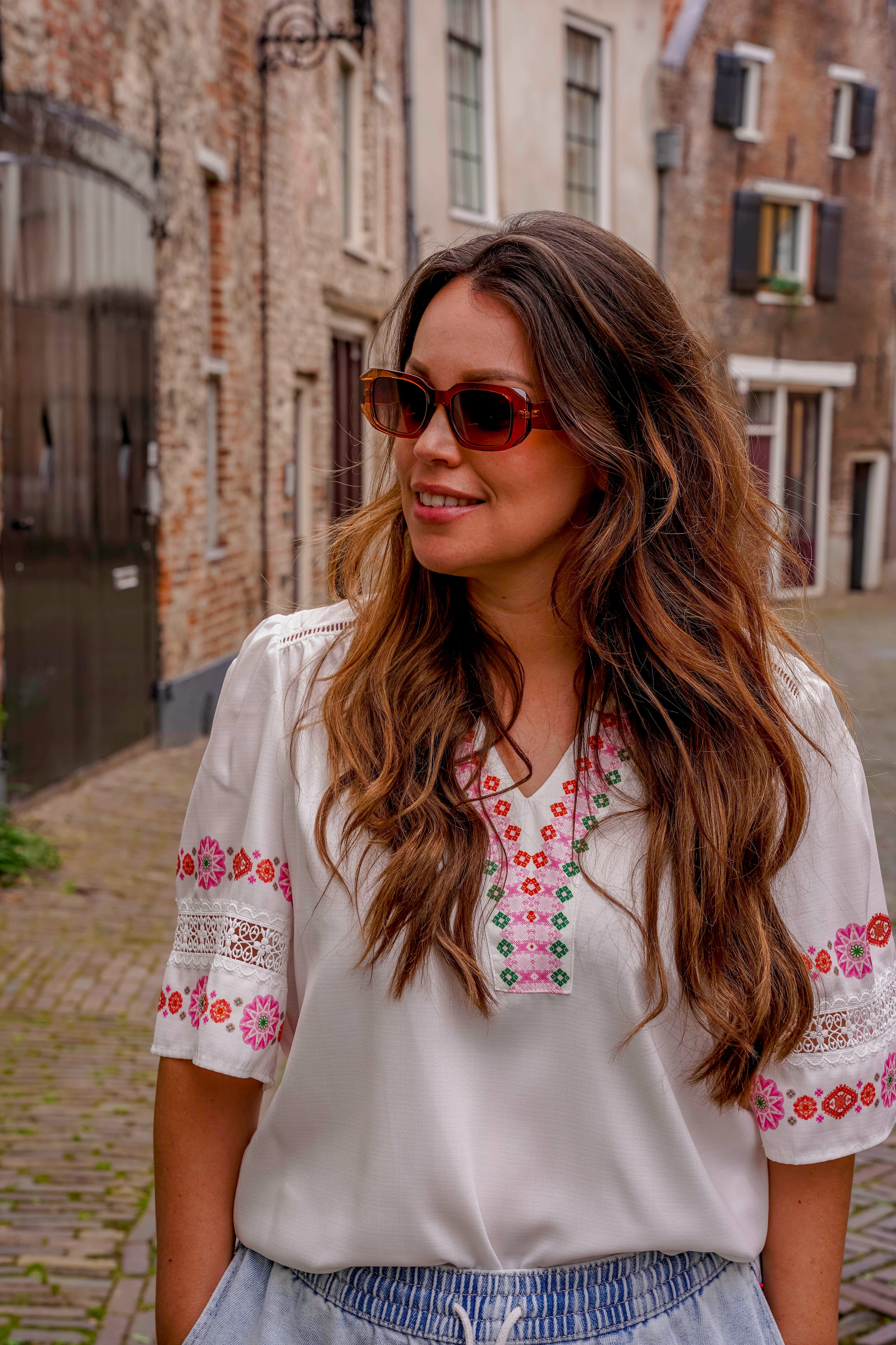 Vrouw met stijlvolle zonnebril en geborduurde blouse in straatje
