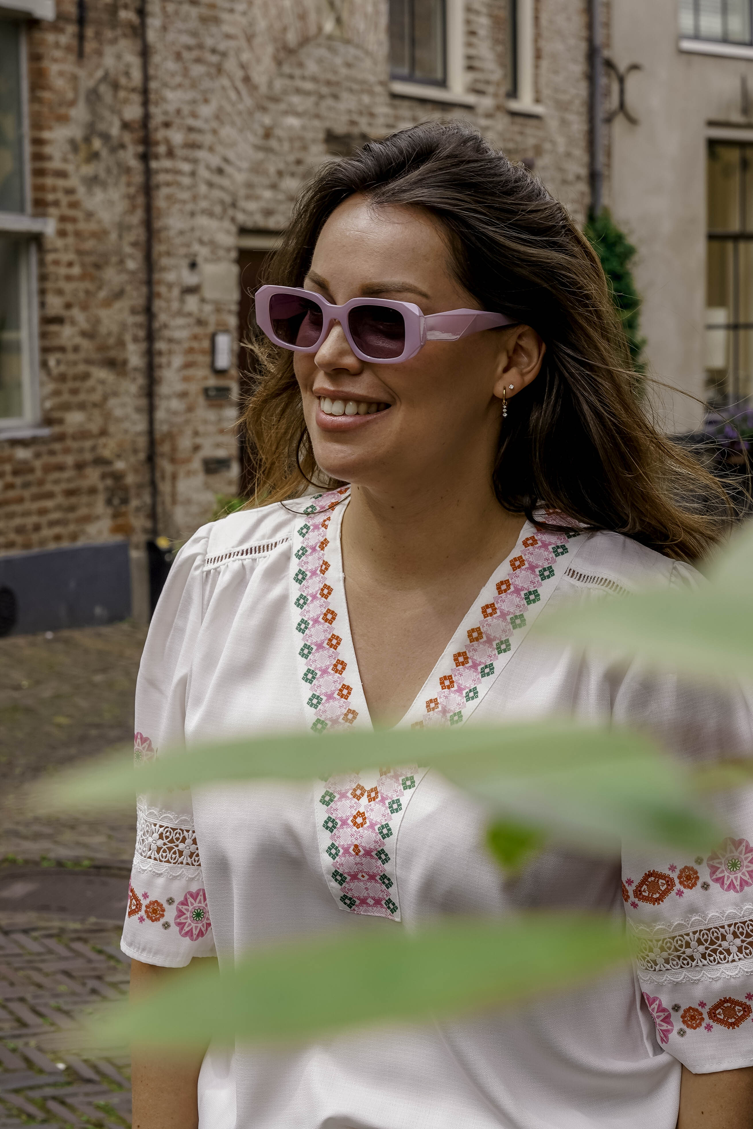 Vrouw met stijlvolle paarse zonnebril en geborduurde witte blouse, perfect voor zomerse dagen.