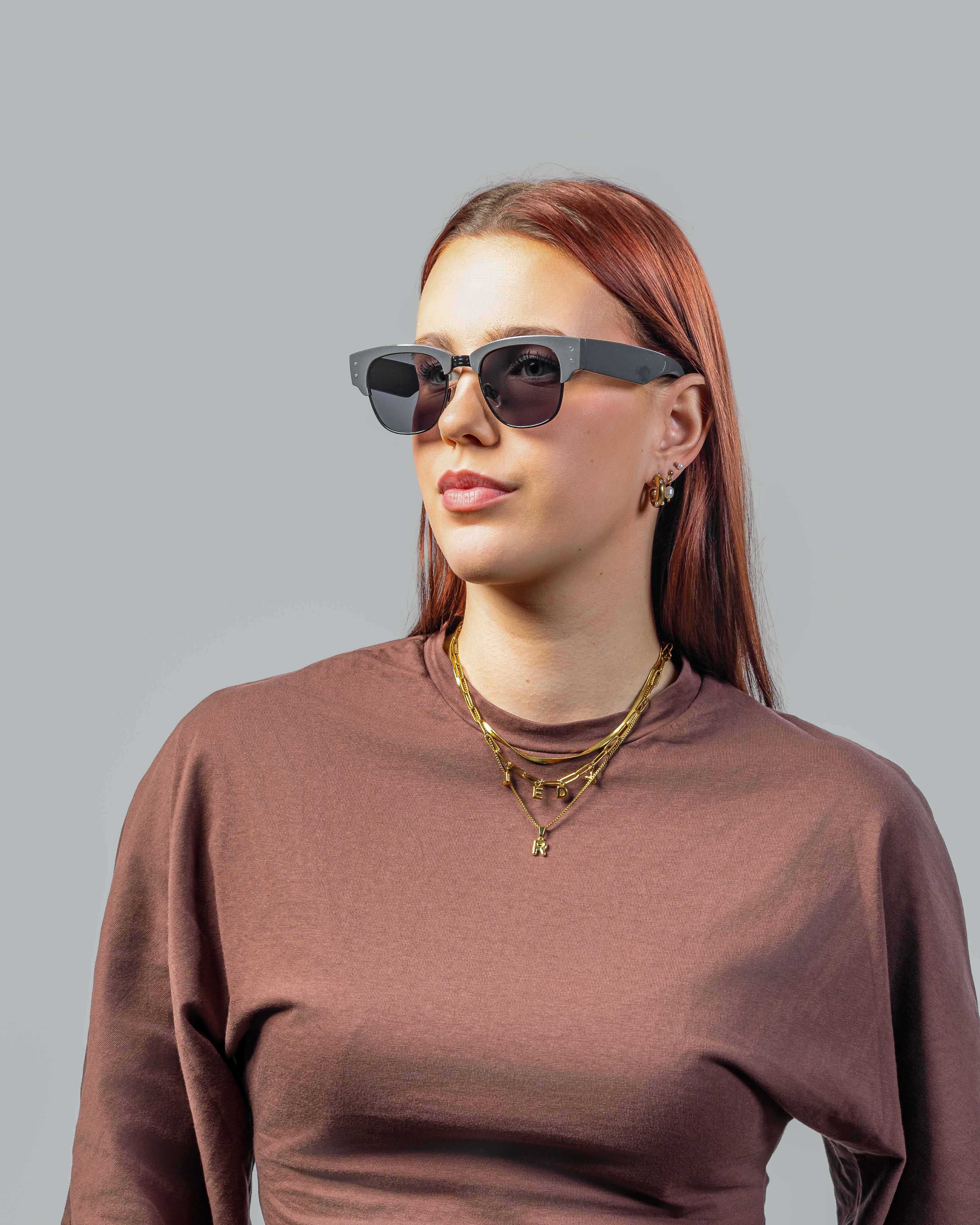 Vrouw met stijlvolle zonnebril, grijze montuur en donkere glazen, perfect voor een modieuze look.