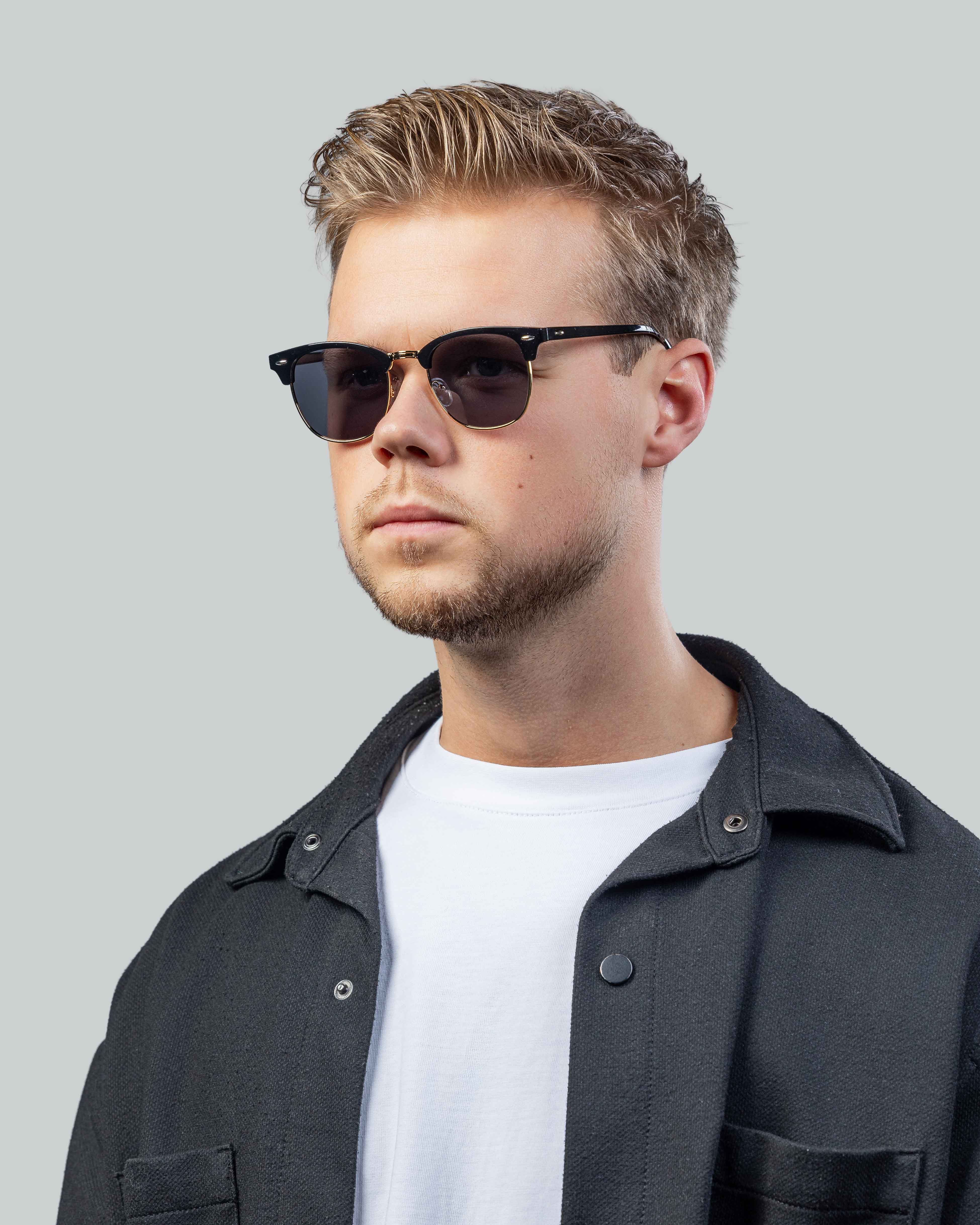 Stijlvolle zonnebril met zwarte montuur en gouden details, gedragen door man in casual outfit