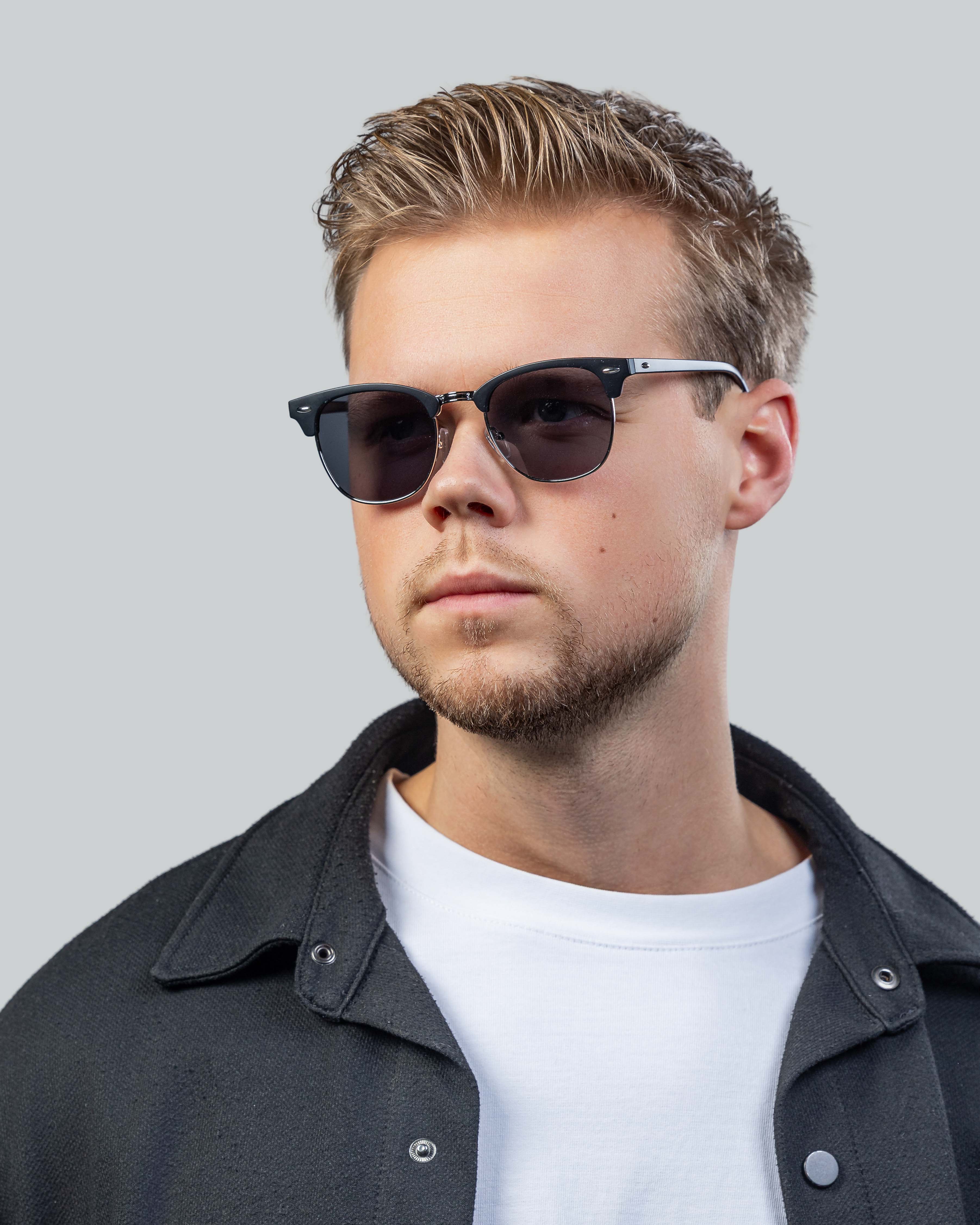Stijlvolle zonnebril met zwarte montuur en donkere glazen, gedragen door man in casual outfit