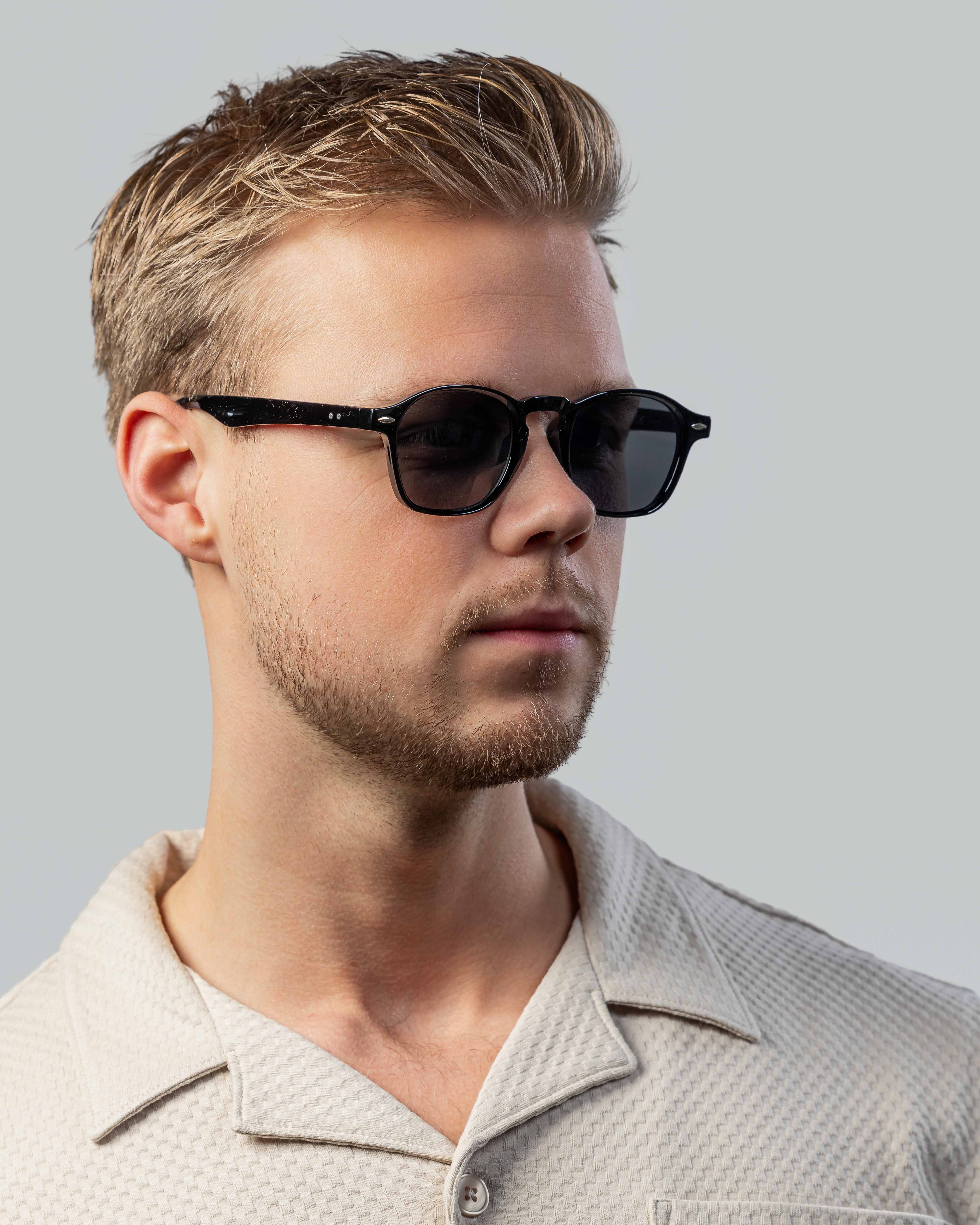Stijlvolle zwarte zonnebril met klassiek design, gedragen door man met kort haar en lichte baard.