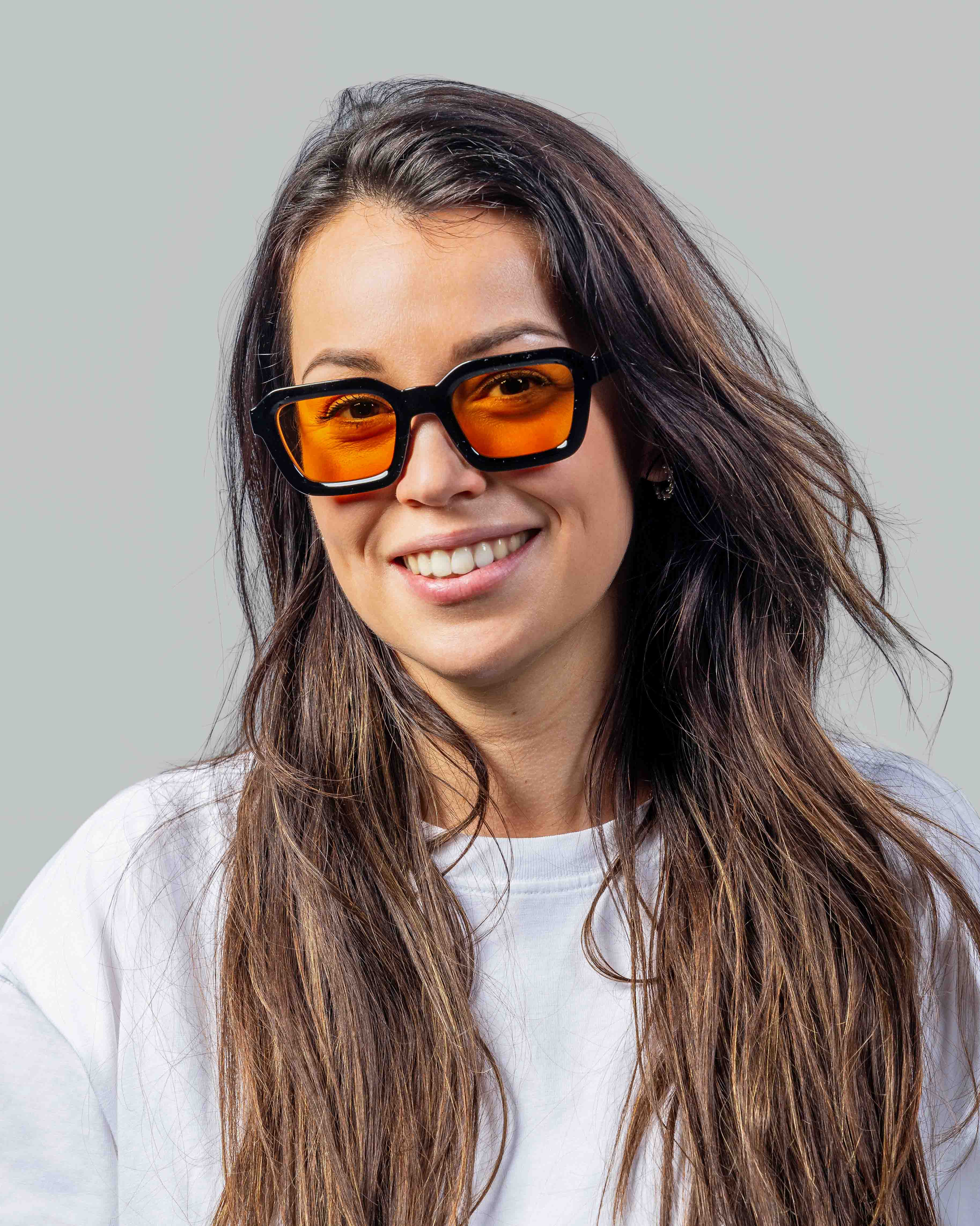Vrouw met stijlvolle zonnebril met oranje glazen en zwarte montuur, perfect voor een trendy look.
