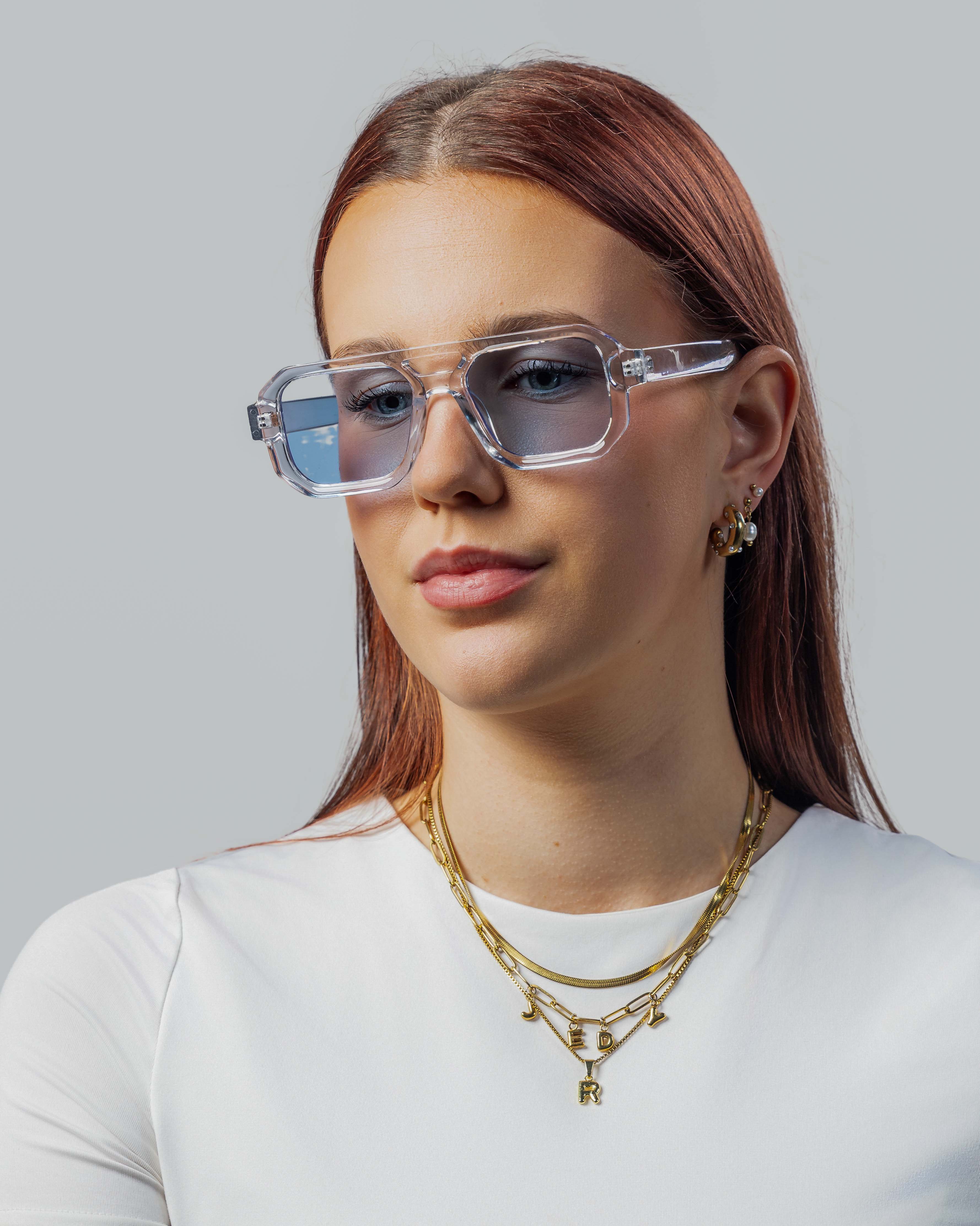 Vrouw met stijlvolle, transparante zonnebril met blauwe glazen en gouden sieraden