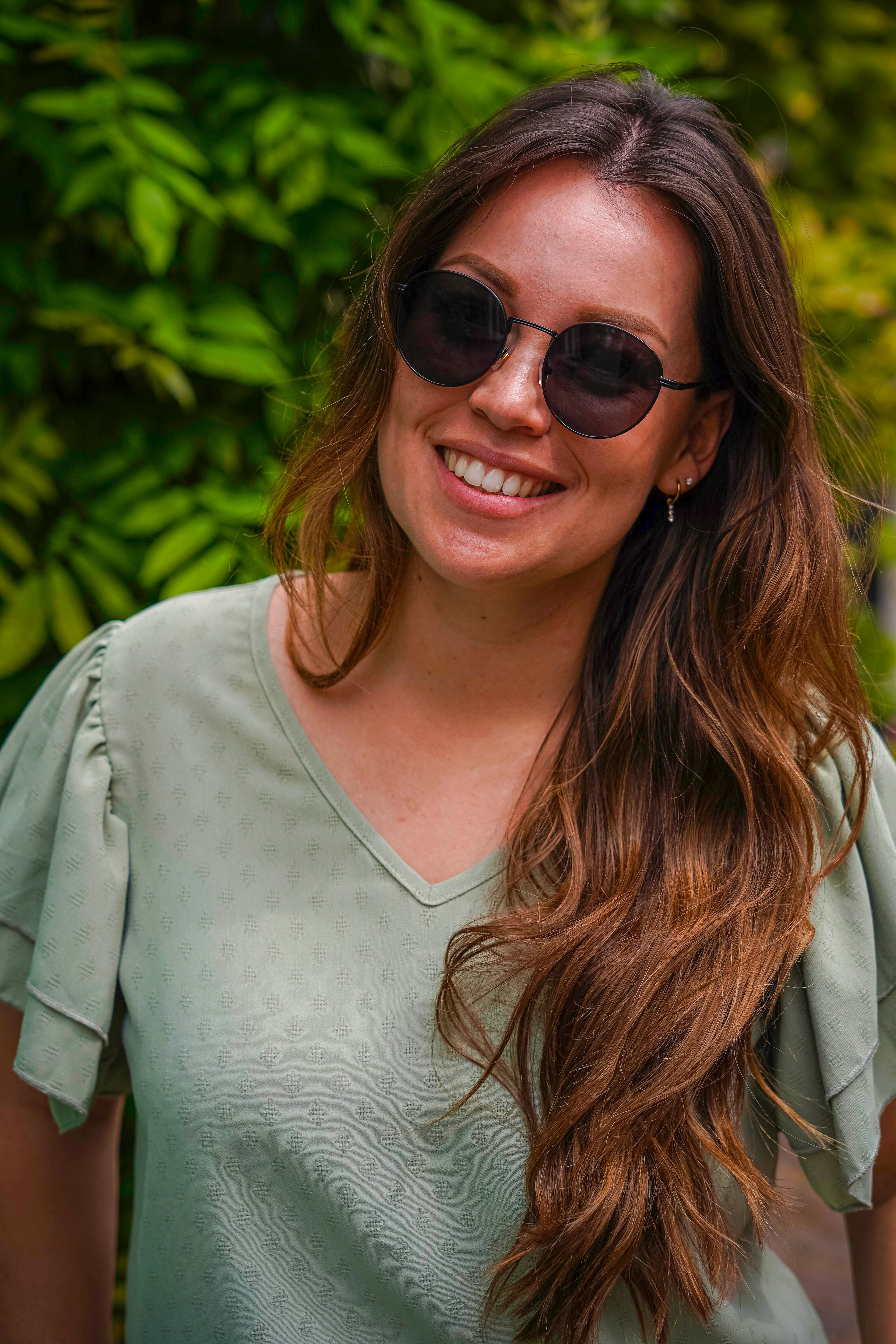 Vrouw met ronde zonnebril glimlachend in groene tuin, stijlvolle zonnebrillen voor elke dag