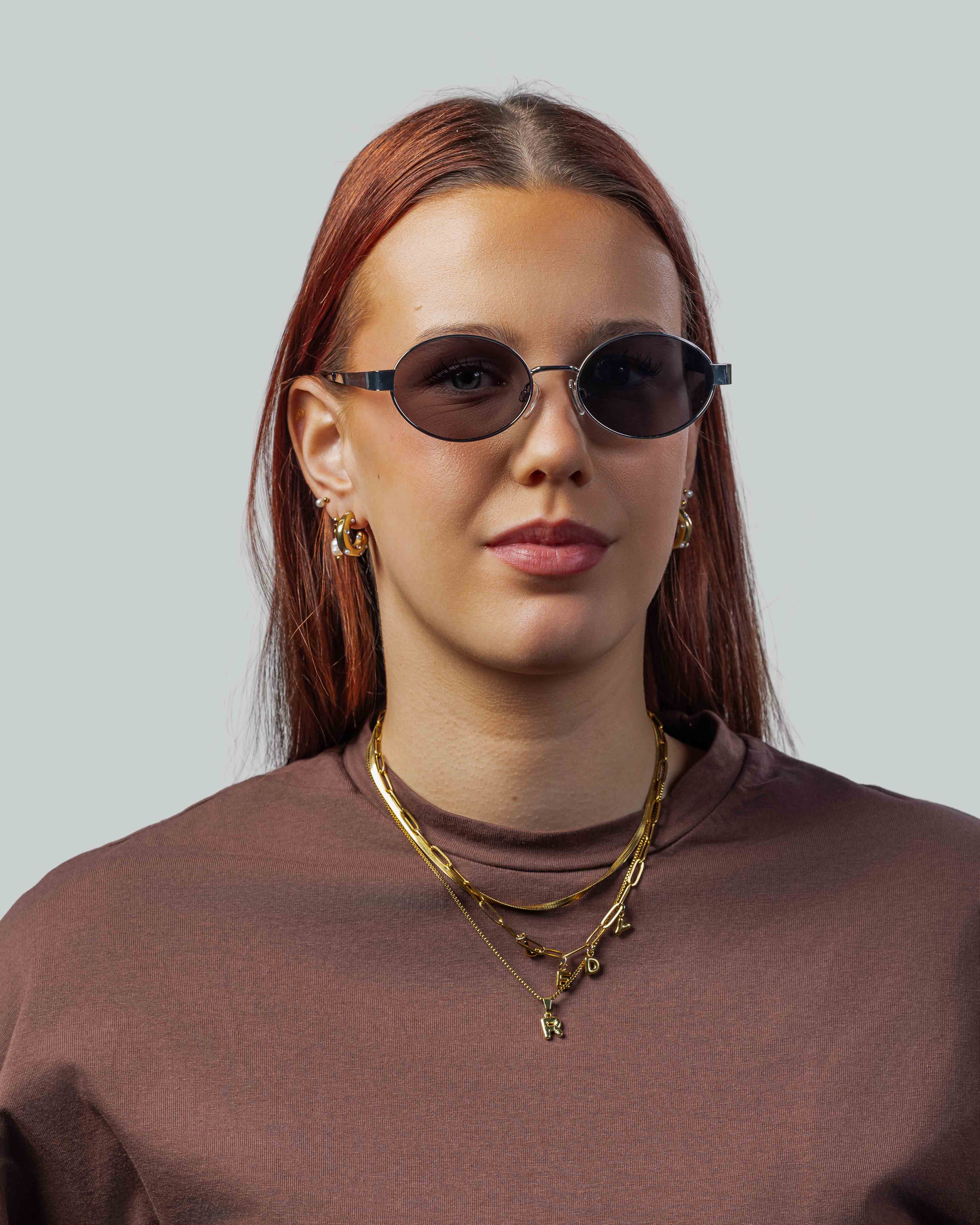 Vrouw met stijlvolle ovale zonnebril, gouden sieraden en bruine trui