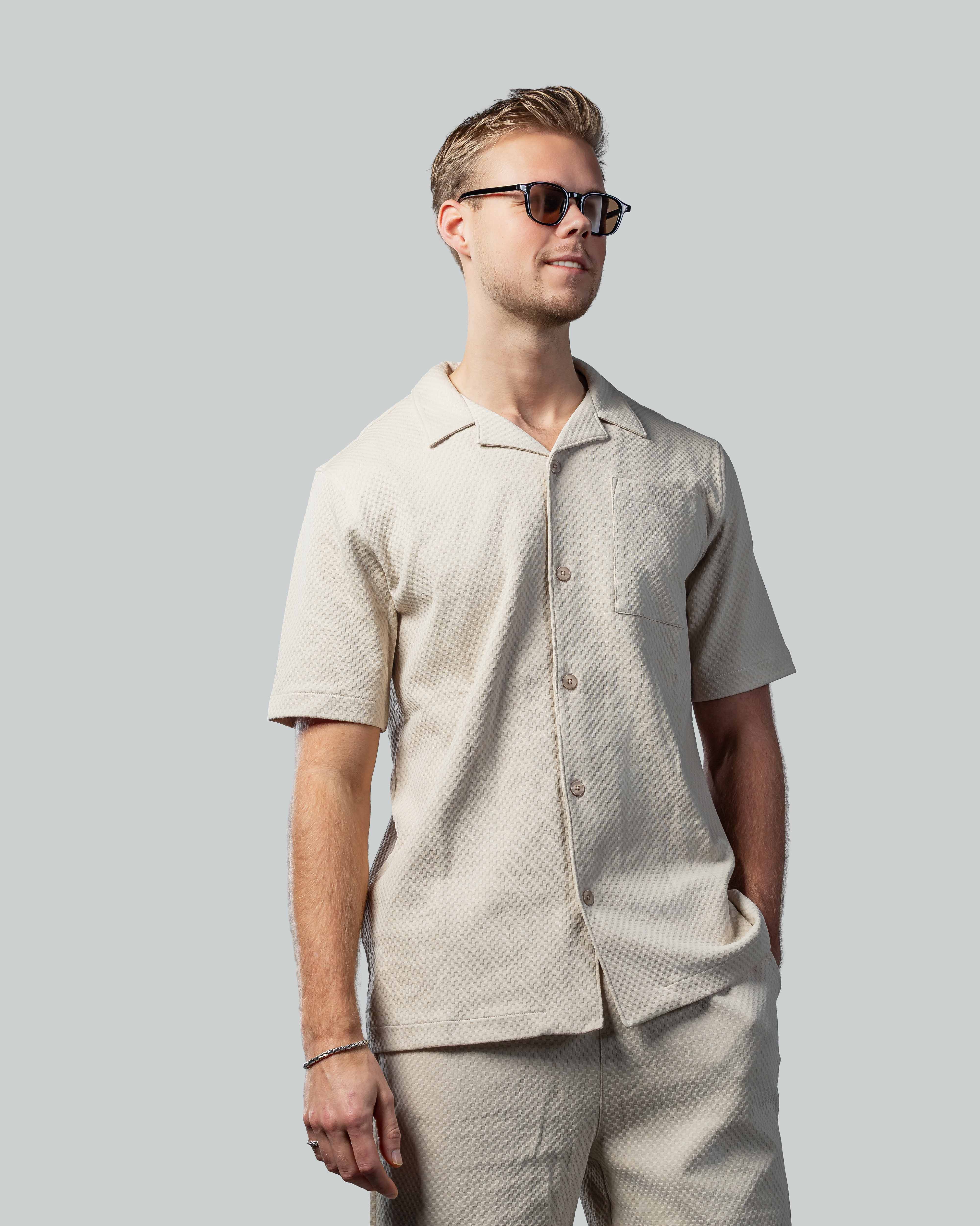 Stijlvolle zonnebril voor mannen, gedragen met beige outfit tegen grijze achtergrond