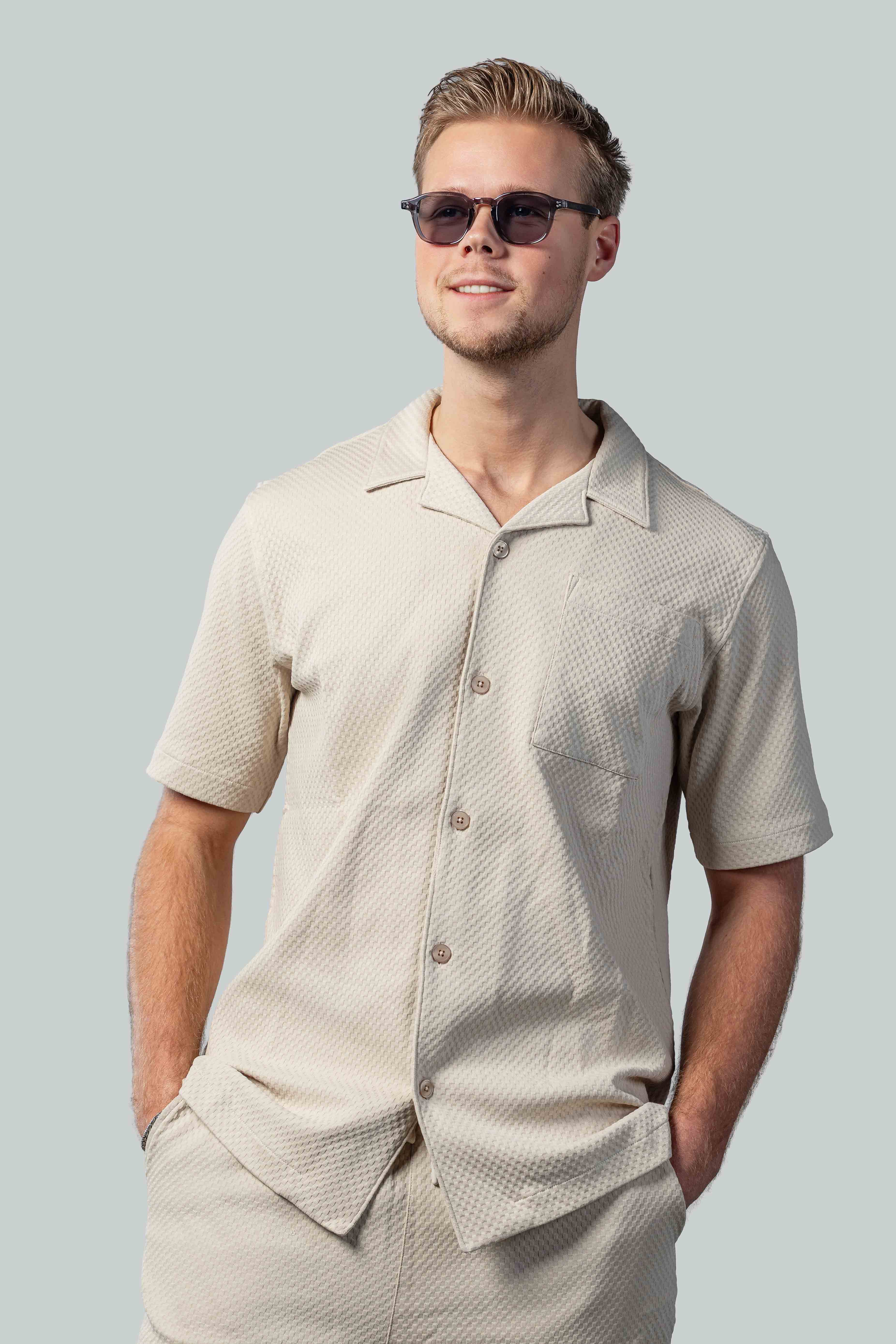 Man met stijlvolle zonnebril en beige overhemd, perfect voor zomerse dagen en zonbescherming.